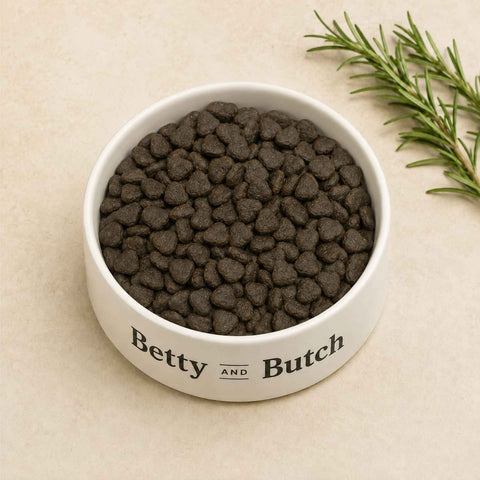 a bowl of peptide dental dog food against a cream background with a sprig of rosemary. 